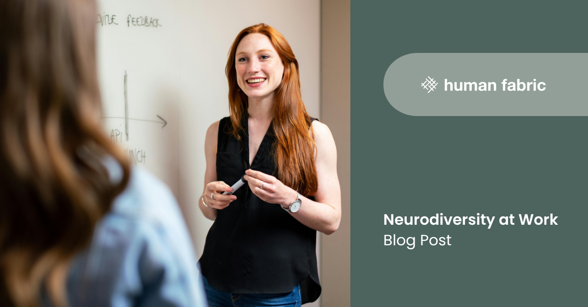 Woman with long red hair holding a marker pen talking to someone in front of a whiteboard