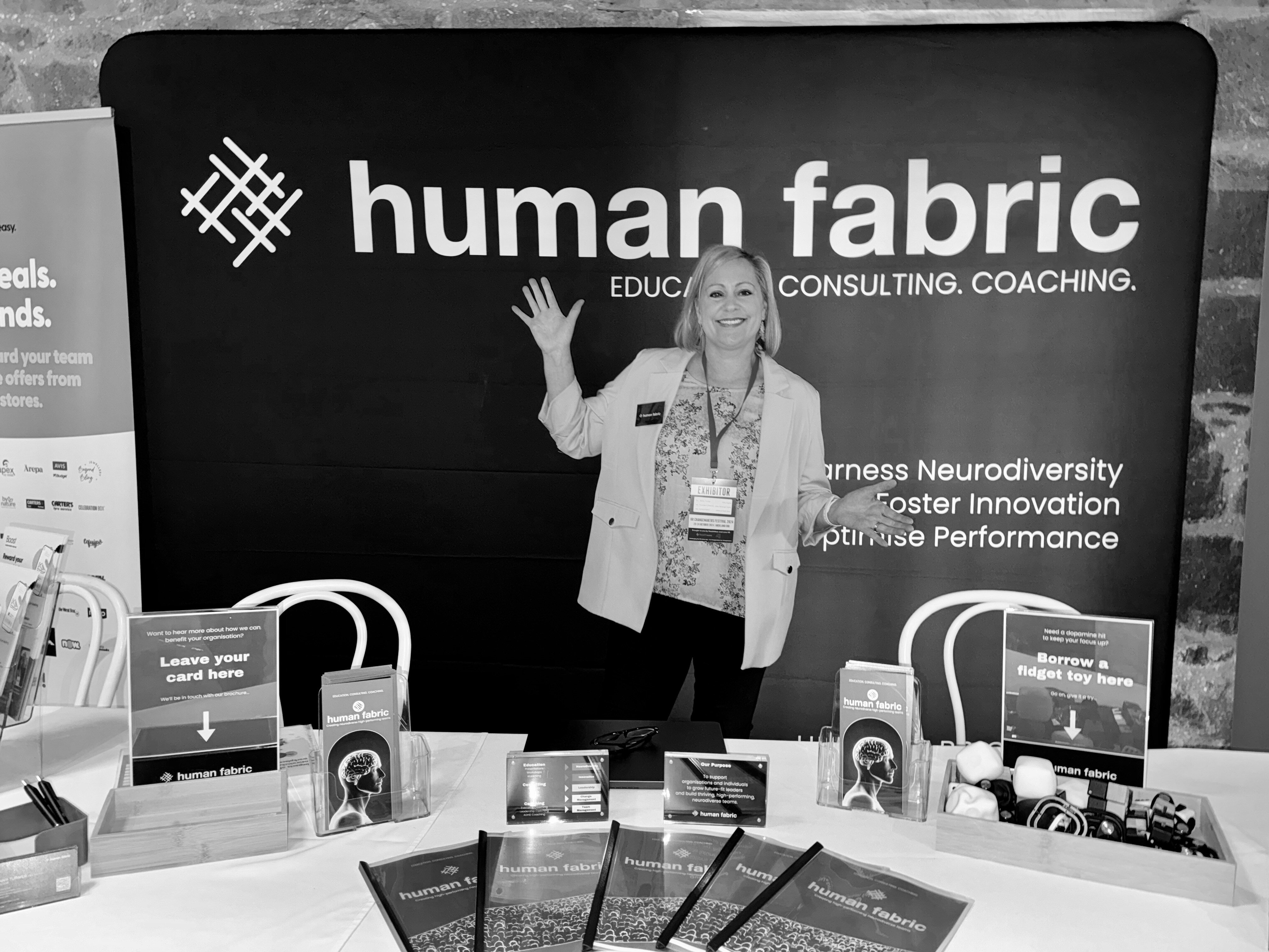 Jenny Turner welcoming people to the Human Fabric stand at a conference, in front of a large Human Fabric banner