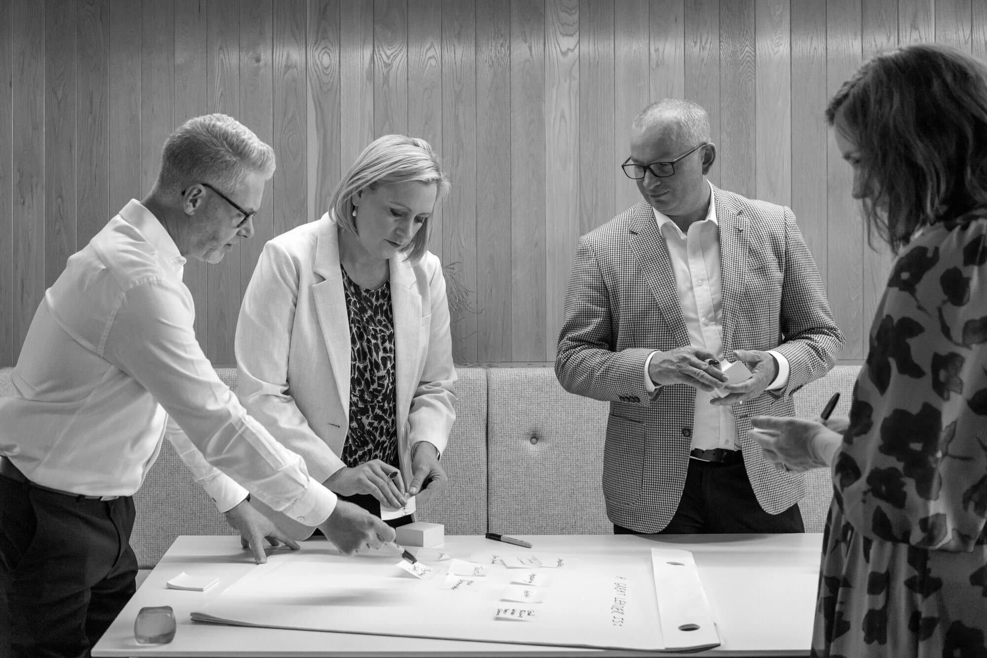 Four people standing around a table in a workshop setting. Four people standing around a table in a workshop setting.