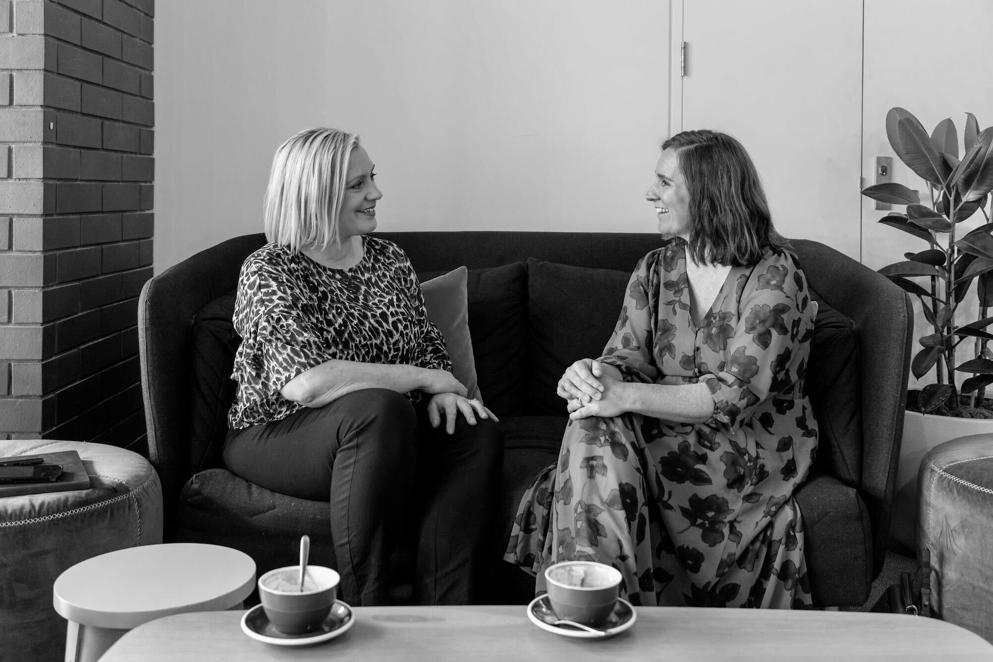 Jenny and a coachee talking on a sofa, with two cups of coffee on a table in front of them.