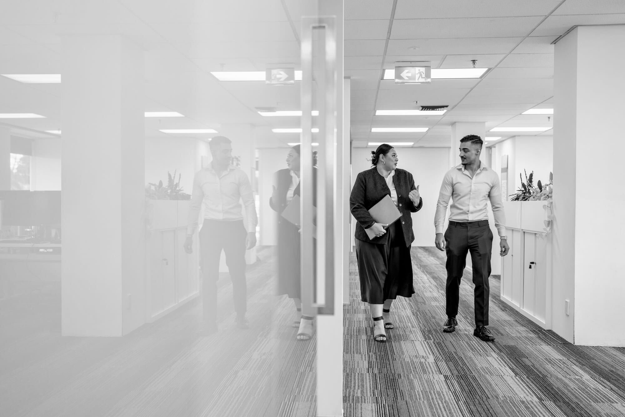 Two people walking along a hallway in a corporate office.