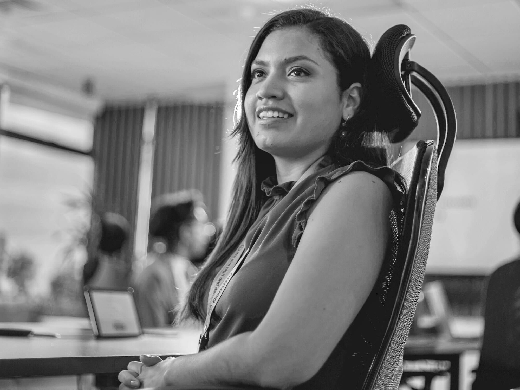 A woman seated at a boardroom table smiling at someone out of the picture.