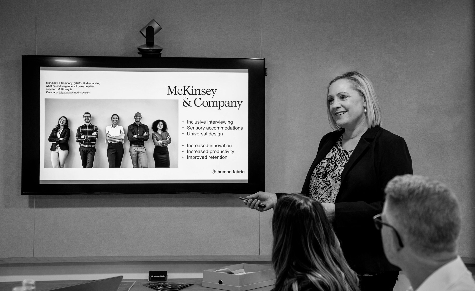 Jenny presenting in a small meeting room, with a slide on the screen about neurodiversity inclusion at McKinsey and Company.