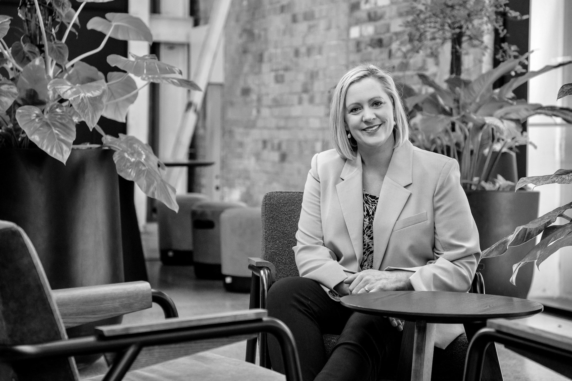 A picture of neurodiversity consultant Jenny Turner sitting on a chair, looking relaxed, surrounded in indoor plants.