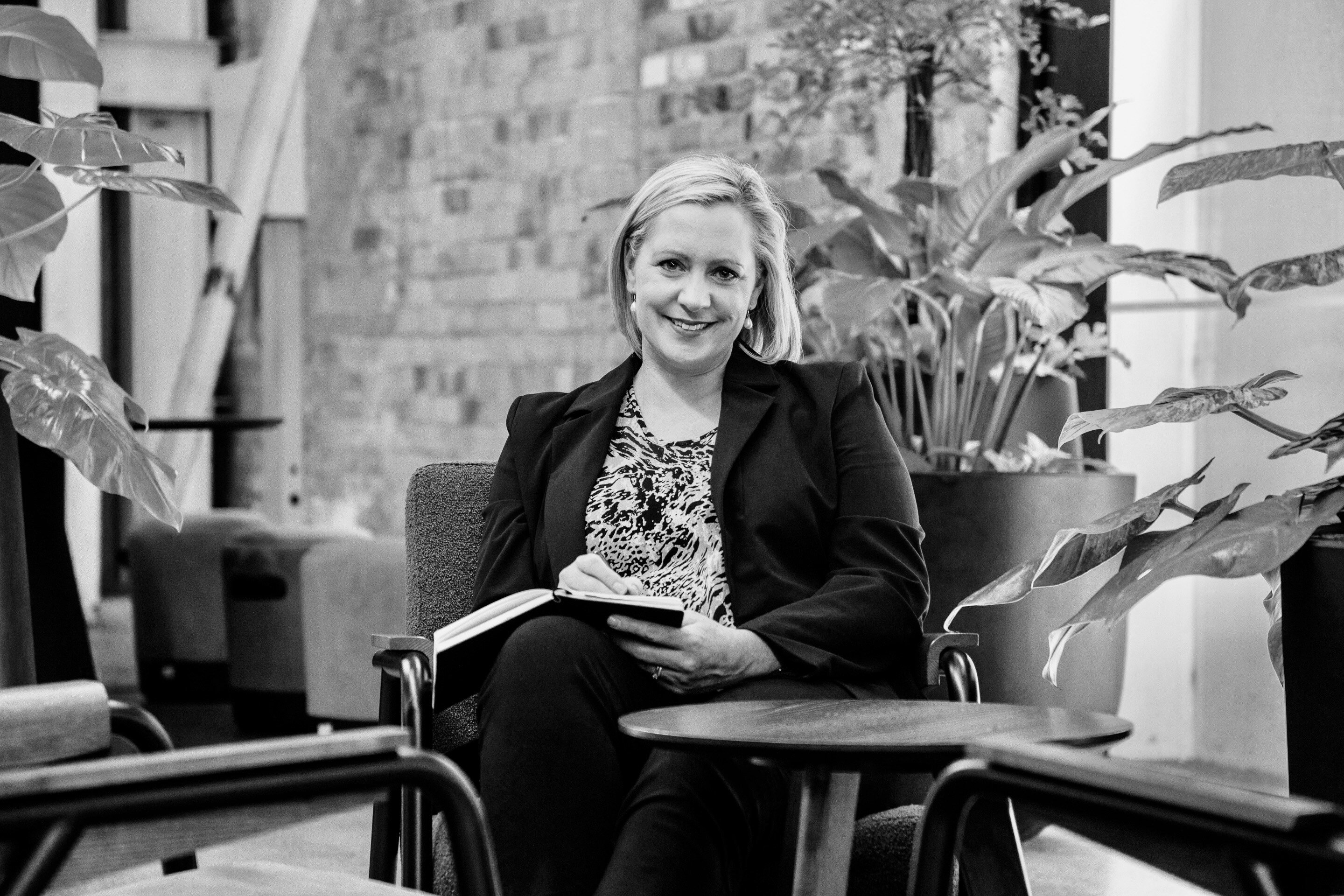 Jenny sitting at a coffee table with a notebook and pen, smiling at the camera