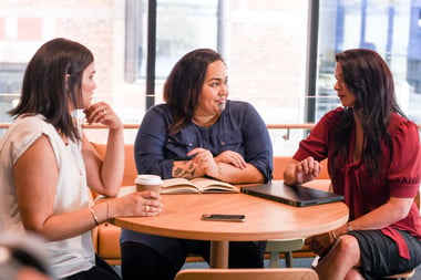 Three NZ woman sitting at a round table talking.