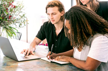 Two people working in front of a laptop, with a third looking over them.