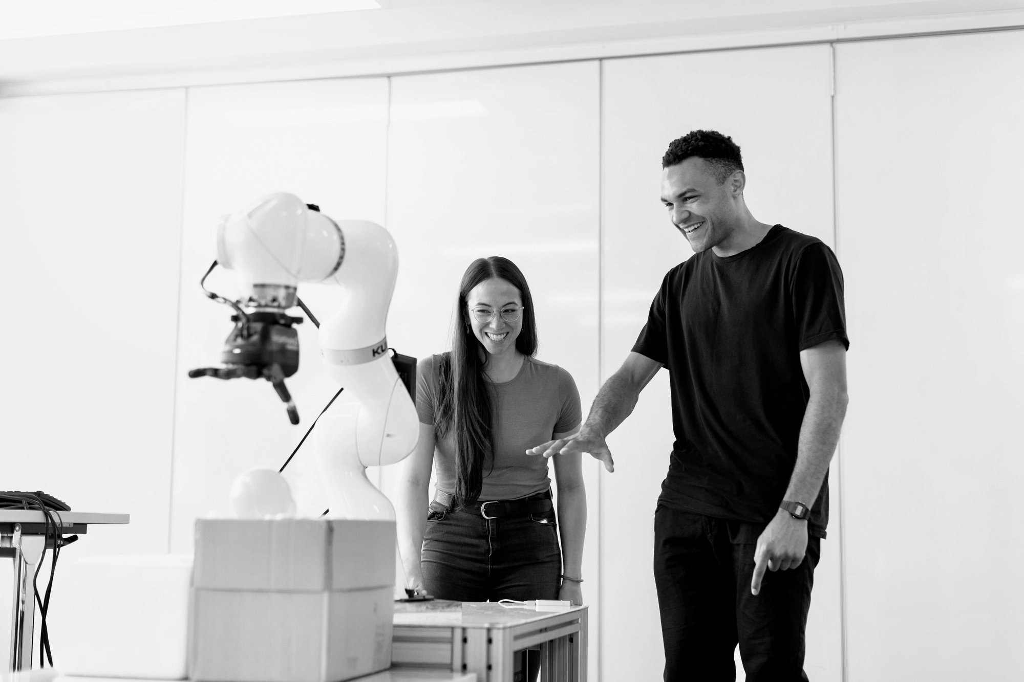 A woman and a man in front of some robotic technology, laughing.