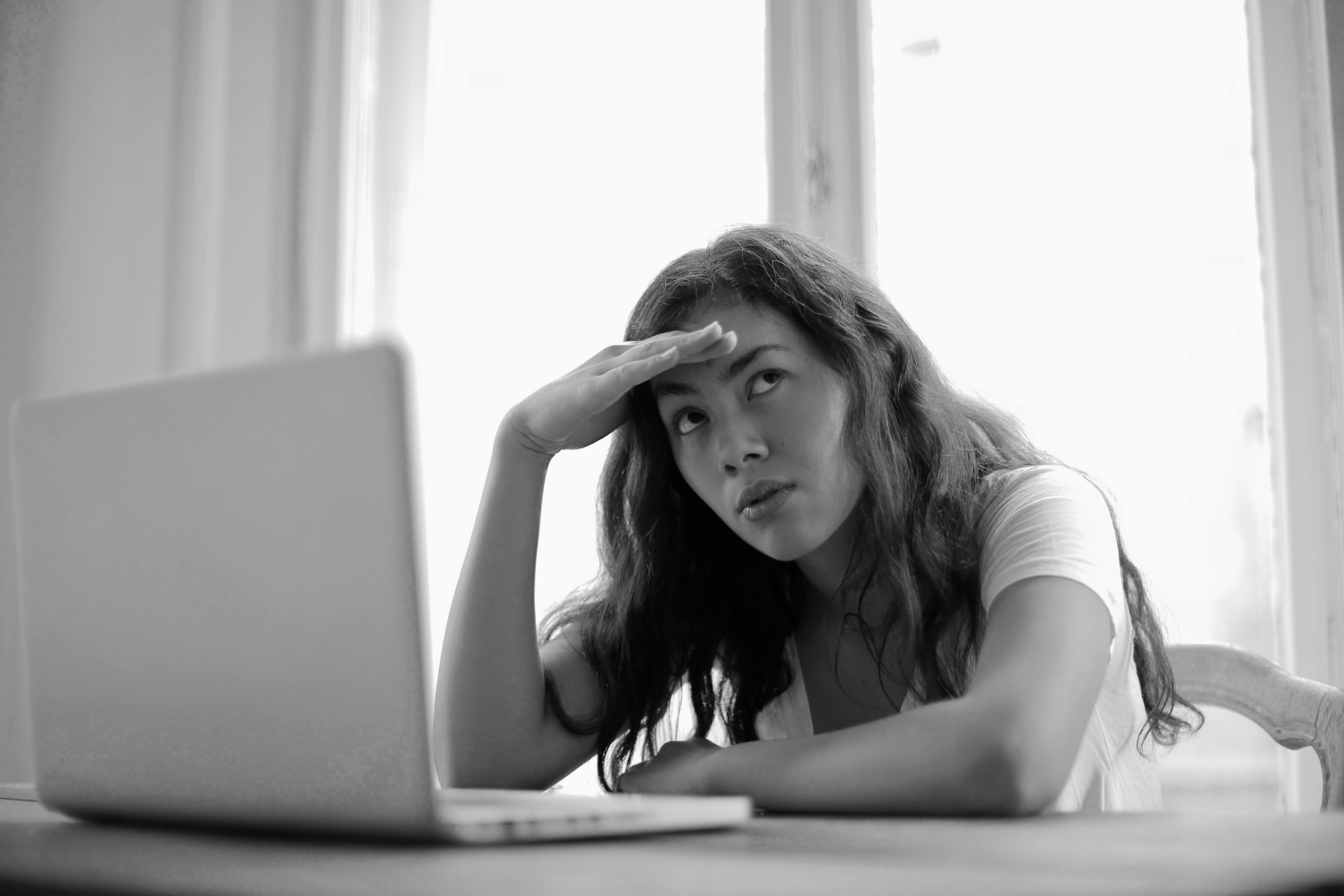 A woman looking frustrated at her computer with her head on her forehead